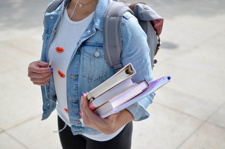 student with a backpack and arm full of textbooks